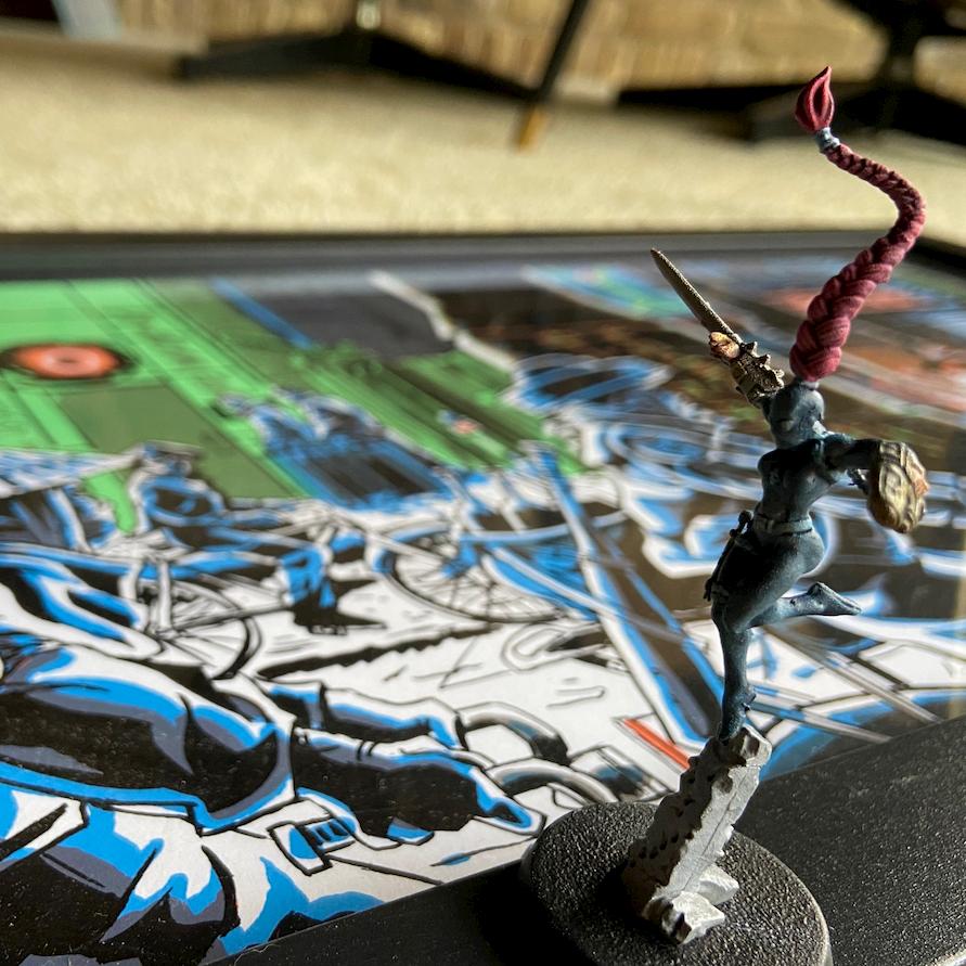 An athletic looking gaming miniature, with pink hair, standing on a Tim Doyle art piece of Blade Runner